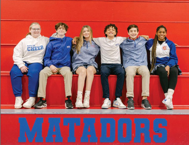 students smiling on a gym bleacher bench